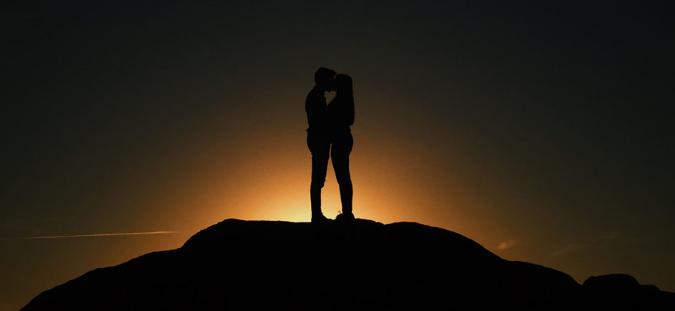 To personer som kysser foran soloppgangen