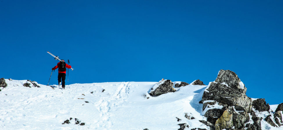 Person med ski over skuldrene står på toppen av snødekt fjell