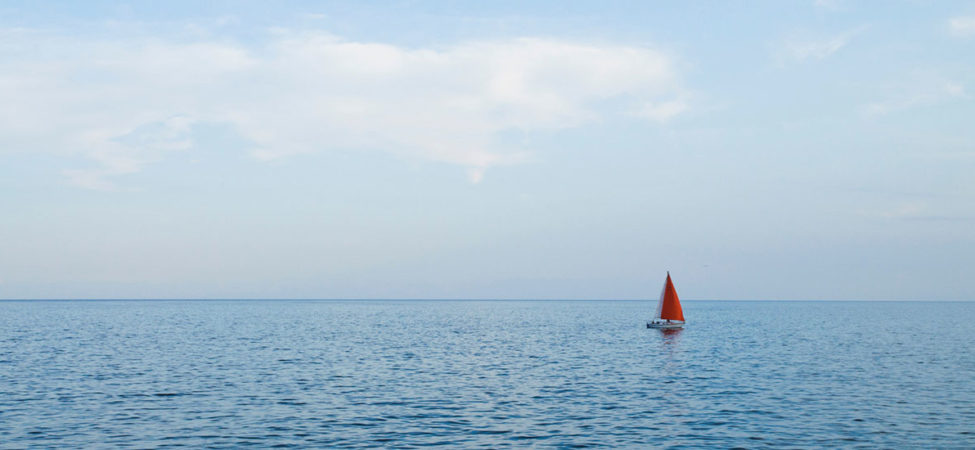 Liten seilbåt med rødt seil alene på vannet - Illustrasjonsfoto