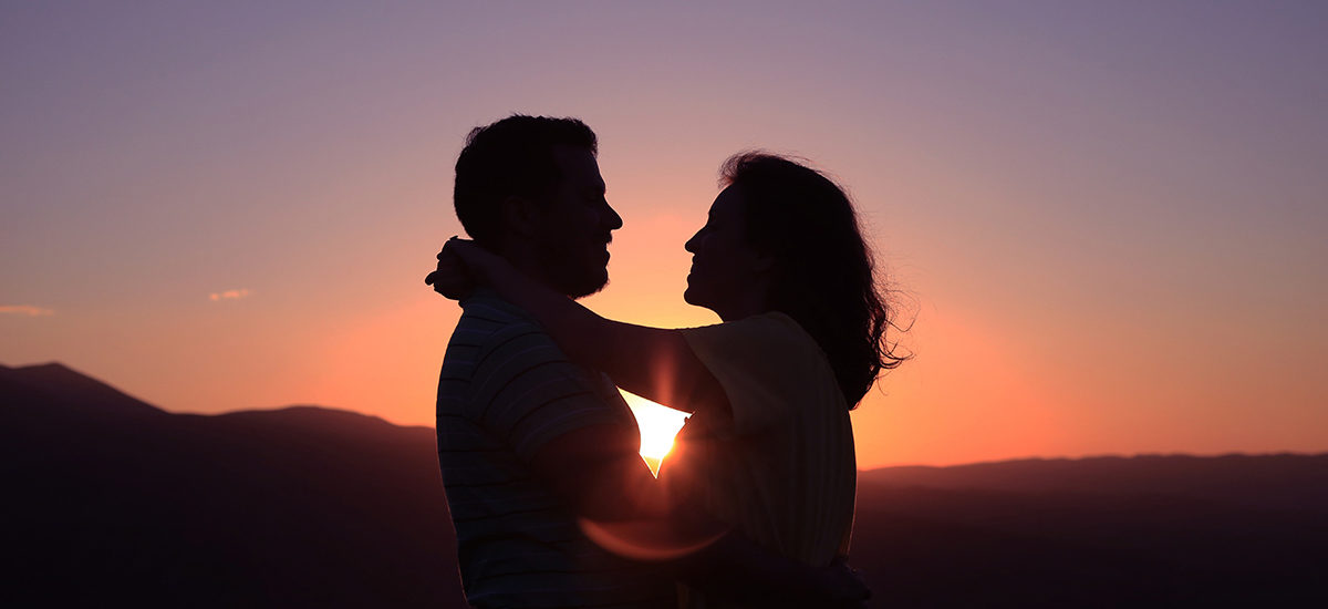 To personer som holder rundt hverandre med solnedgang i bakgrunnen