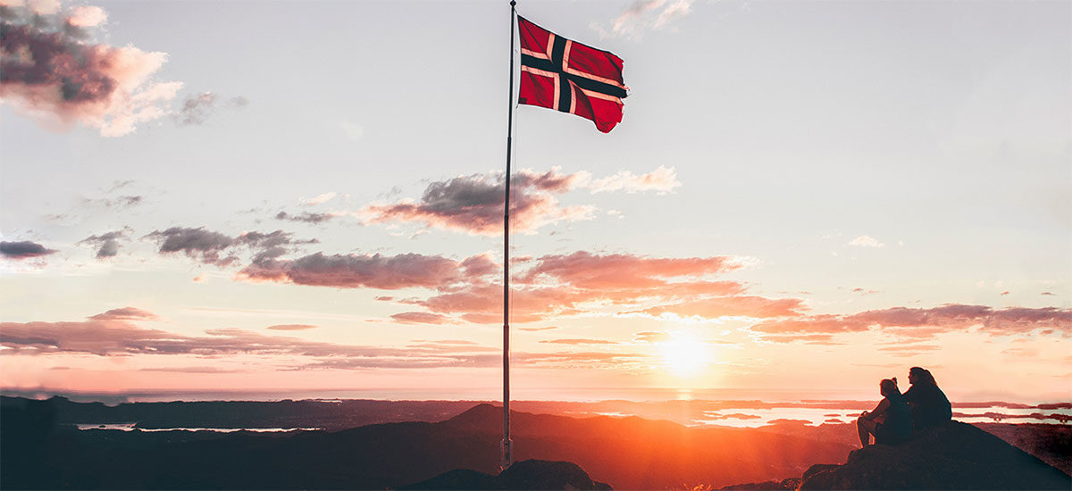 Norsk flagg på flaggstang med solnedgang i bakgrunnen