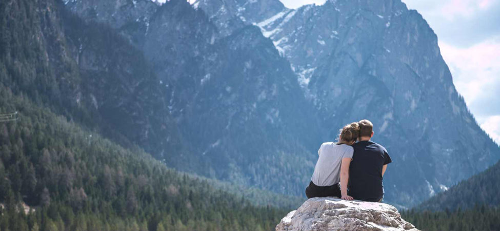 To personer sitter sammen foran fjord og fjellandskap og lener hodet på hverandre