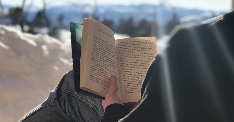 Foto av en som leser bok ute i snøen