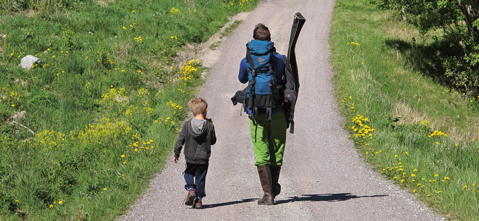 Far og sønn går sammen ned en landeveil med tursekk på ryggen