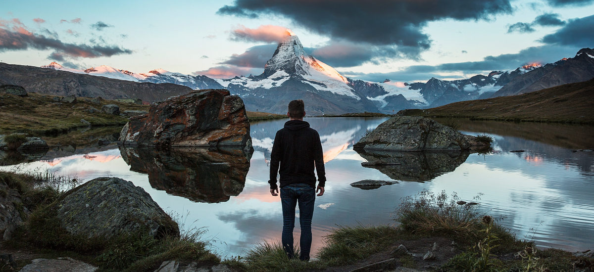 Mann står ved vann i marka og ser på et fjellandskap
