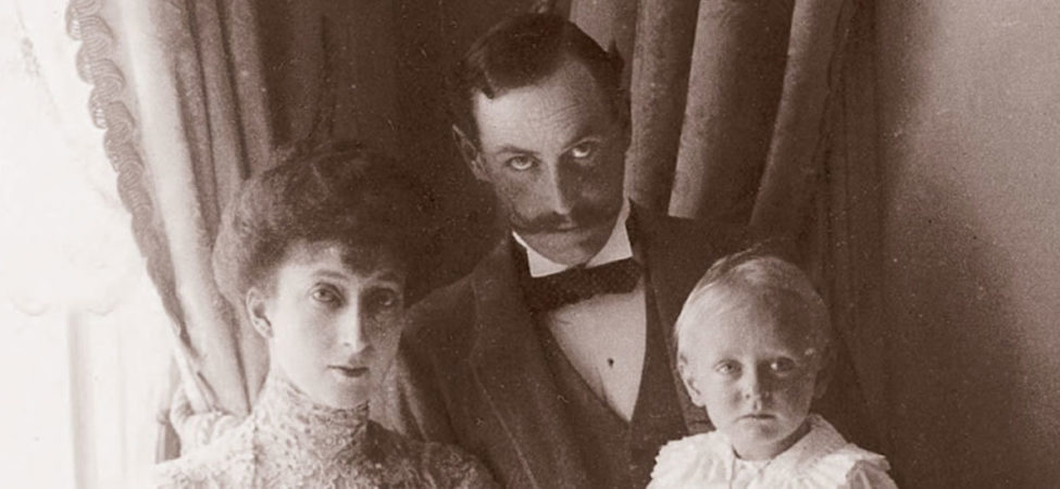Gammelt arkivfoto av Kong Haakon VII og Dronning Maud med lille kronprins Olav på fanget. Fra omslaget til andreboka "Folket" i serien Haakon og Maud.