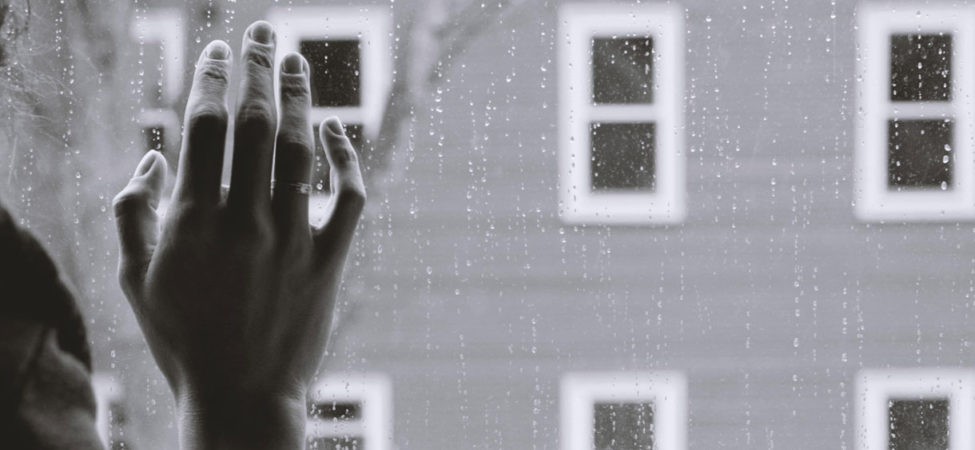 Foto av en hånd som holdes på et vindu, det regner på utsiden.
