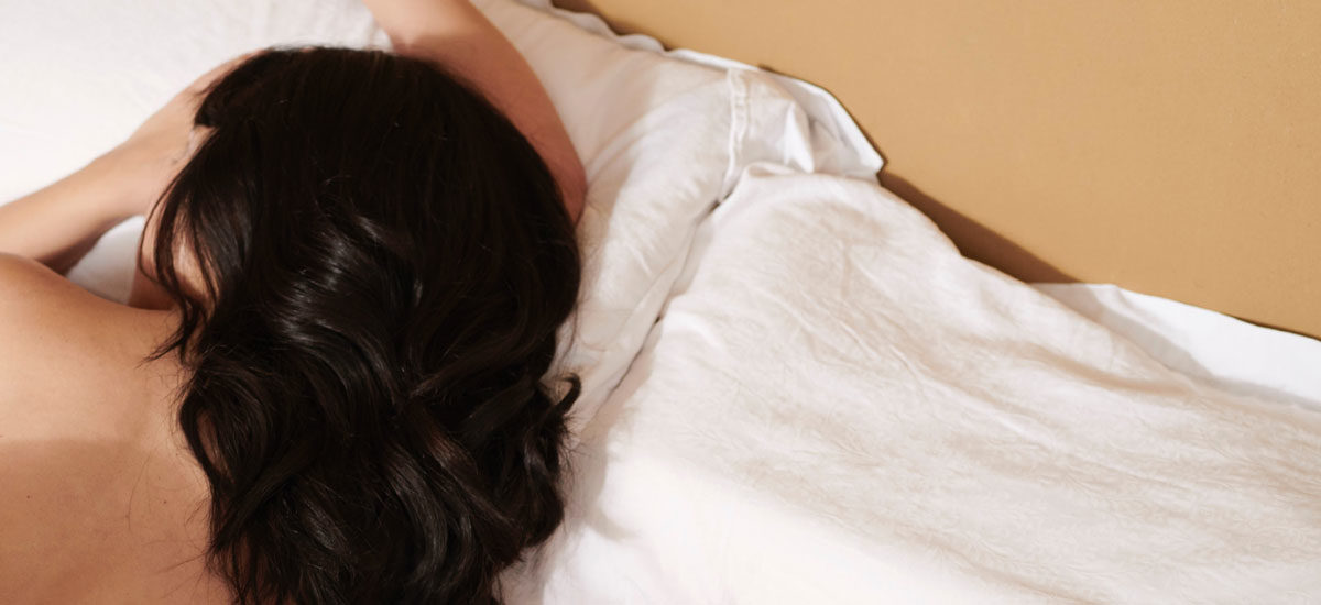 Foto av mørkåret kvinne som sover i en seng.