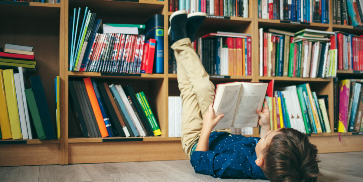 gutt ligger på gulvet foran bokhylle og leser