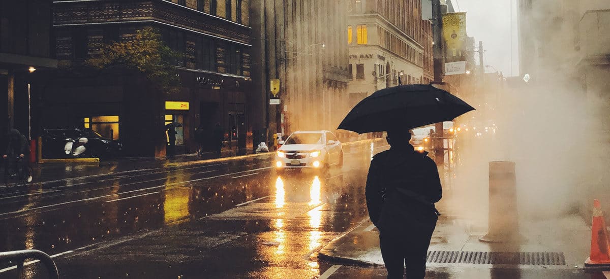Mann med paraply fotografert bakfra i røykfylt gate