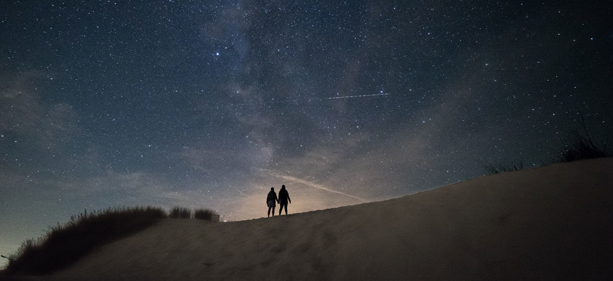 To mennesker holder hender under stjernehimmelen