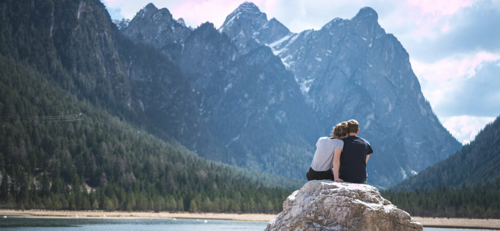 Kjærestepar på en stein ved sjø og høye fjell