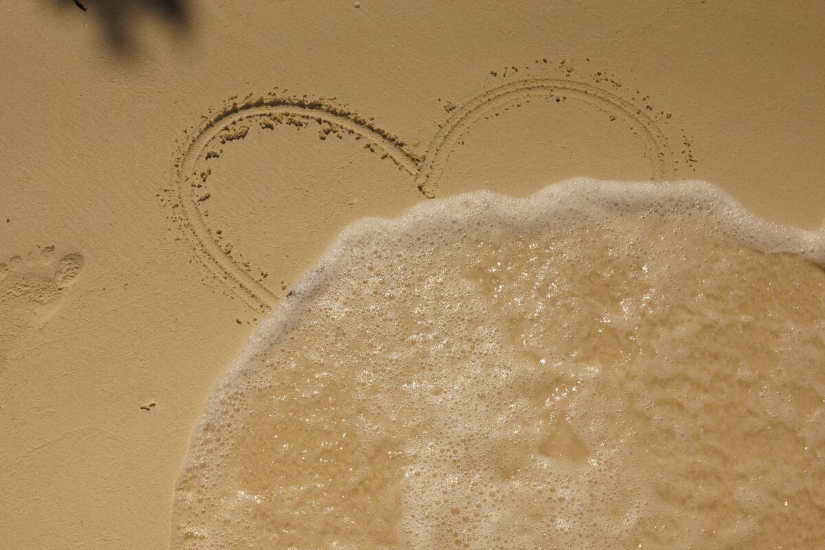 Hjertet i sanden som viskes ut av bølge