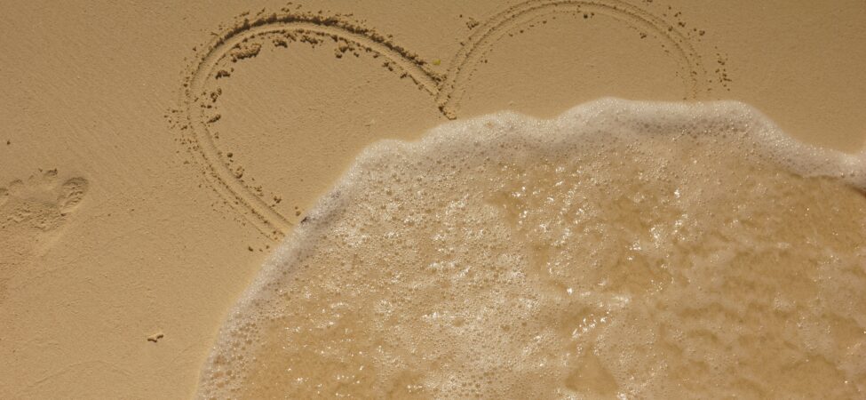 Hjertet i sanden som viskes ut av bølge