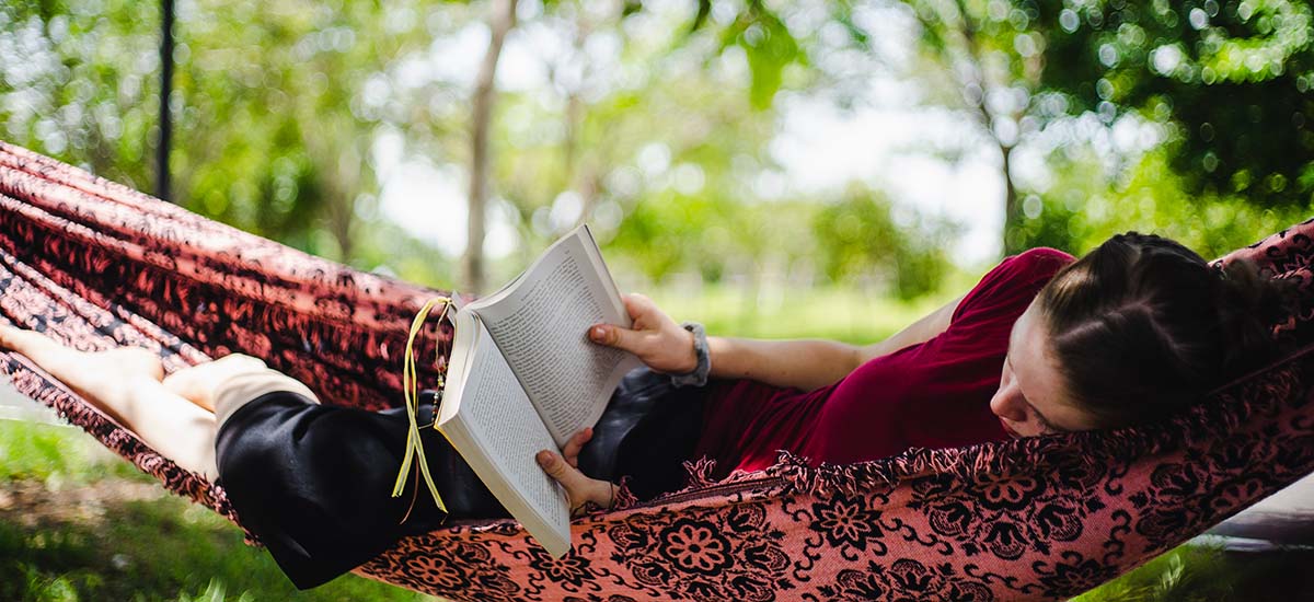 Miljøbilde av en jente som leser bok i en hengekøye