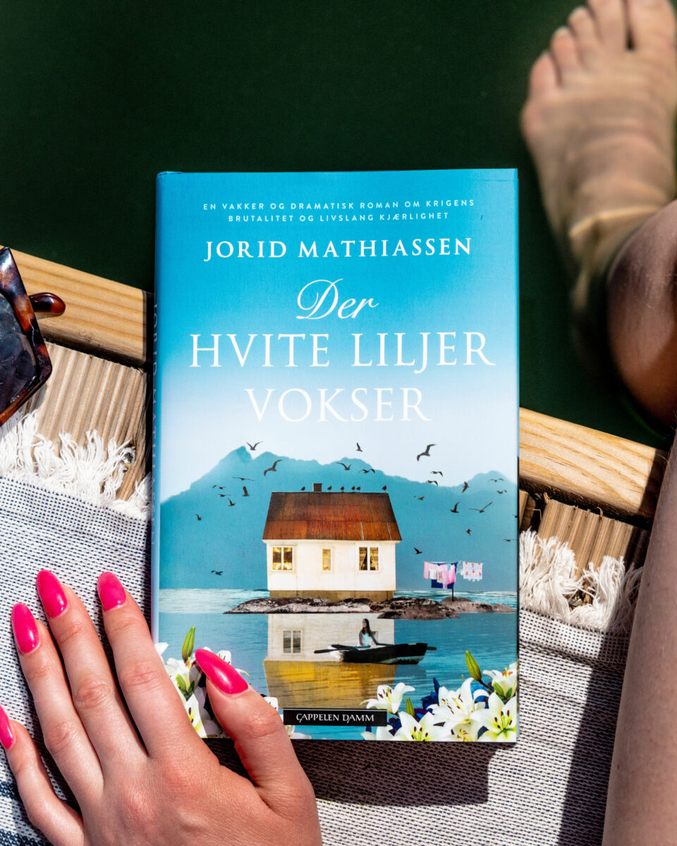 Foto av Jorid Mathiassens roman "Der hvite liljer vokser" på en sommerlig brygge.