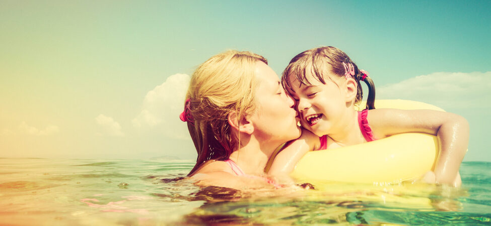 Foto av mor som kysser datter i badering på stranda