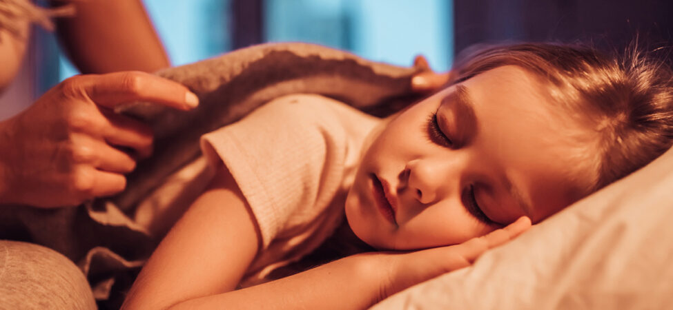 Foto av en som brer over en liten jente som sover