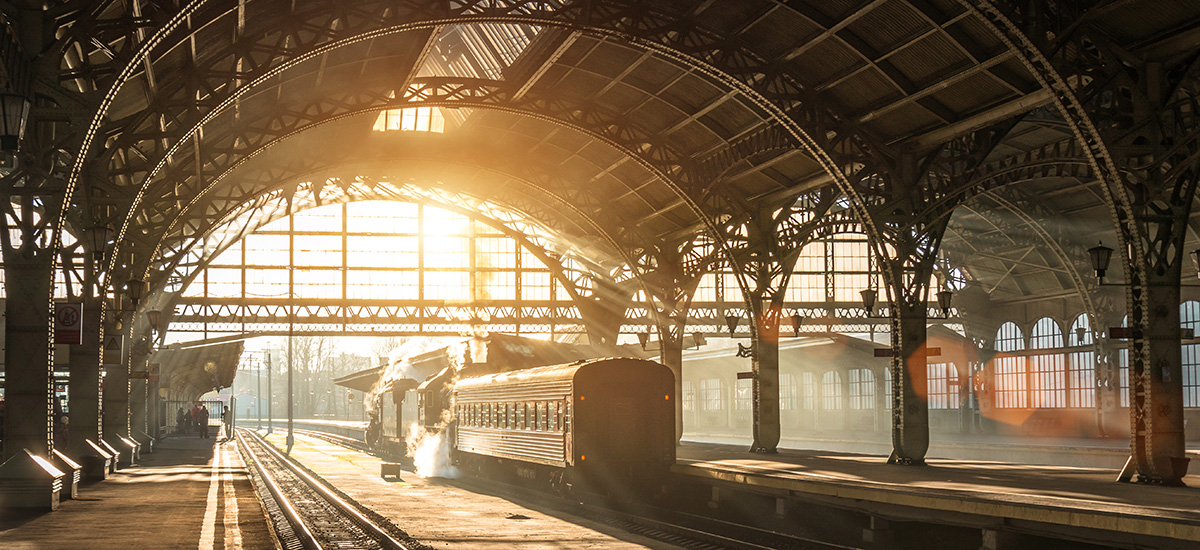 Foto av tog som forlater stasjon i solskinn