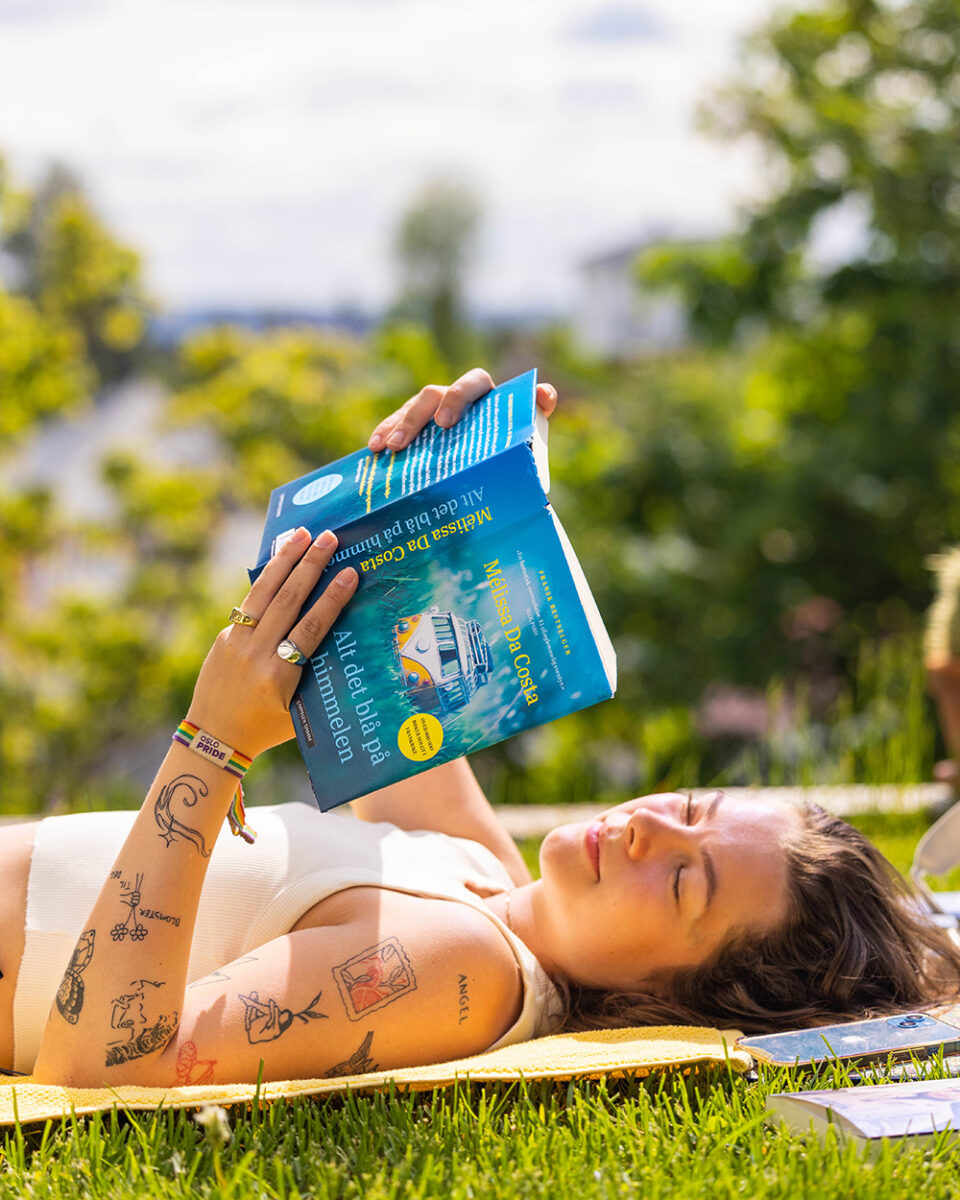 Foto av jente som ligger i en park og leser Mélissa Da Costas bok "Alt det blå på himmelen".