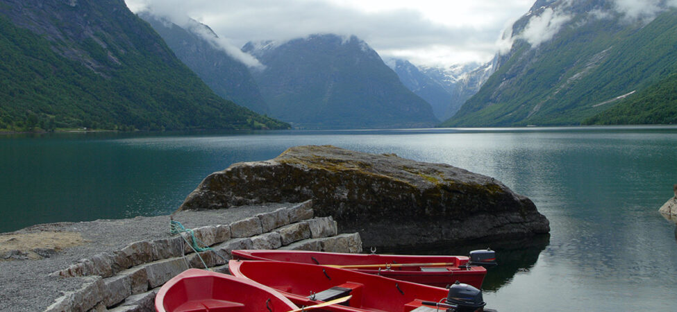 Foto av tre røde båter som ligger fortøyd i en fjordarm. Fjell bak.
