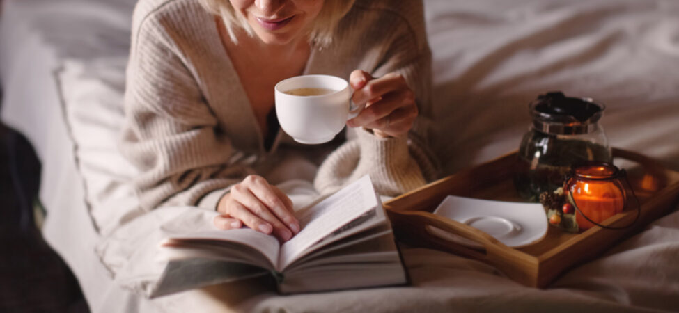 Foto av kvinne som leser og drikker te i senga