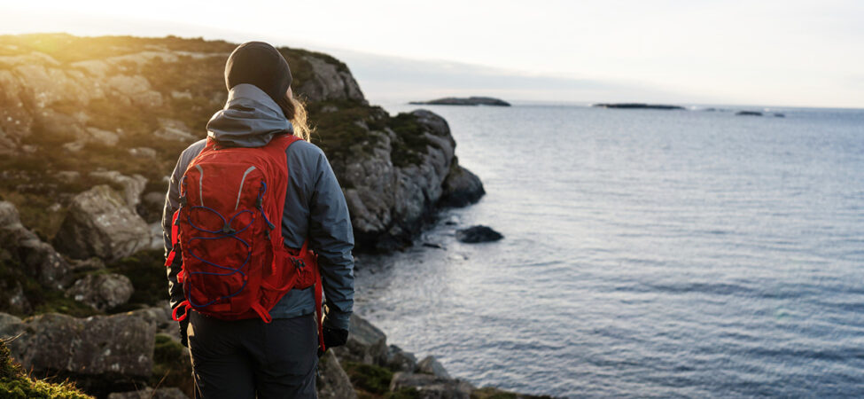 Foto av kvinne med turklær og sekk som ser utover en fjord